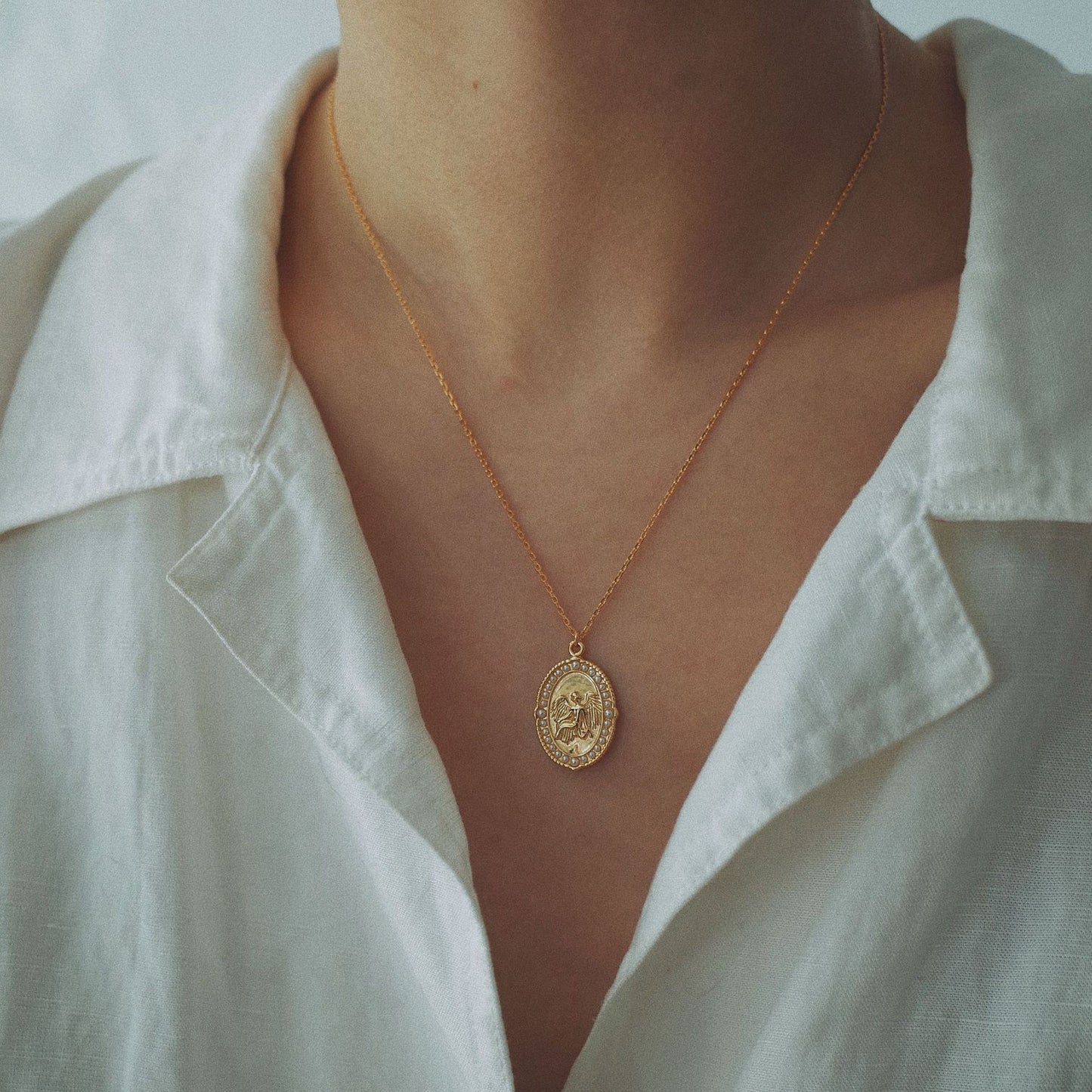 Gold necklace with a pendant worn by a person in a white shirt.