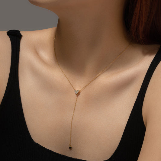 Gold necklace with a heart pendant worn by a person against a neutral background