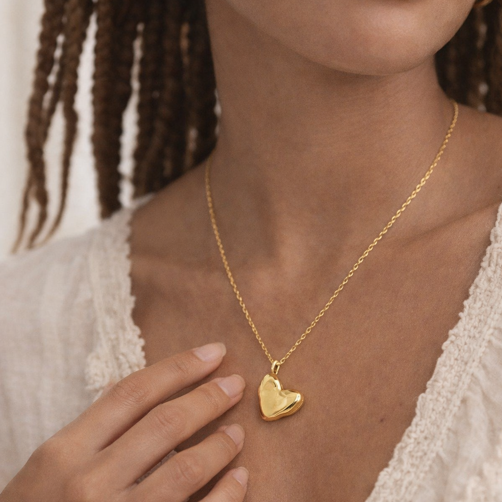 Woman wearing a gold heart-shaped pendant necklace with a plain background