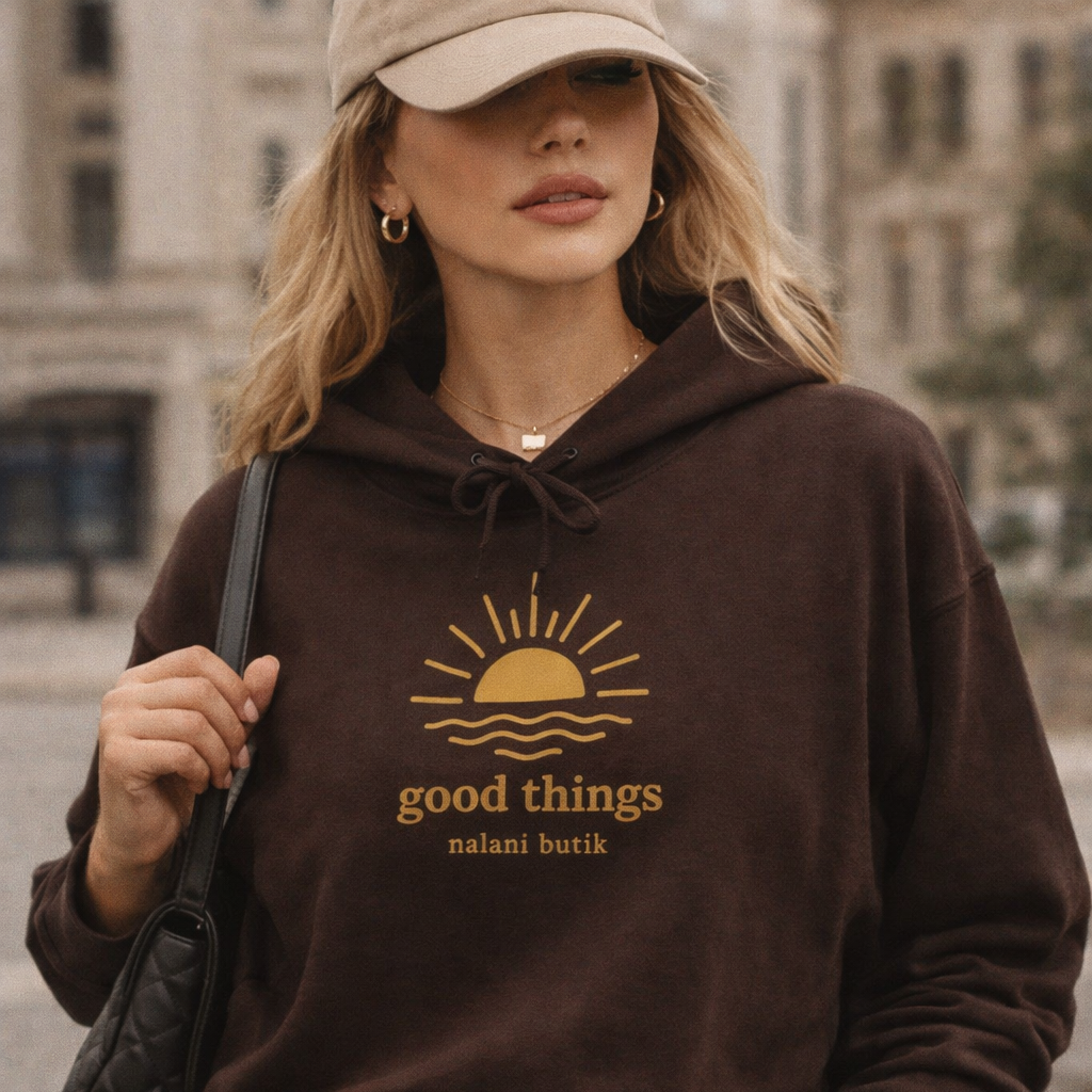 Woman wearing a brown hoodie with a logo and text, standing outdoors.