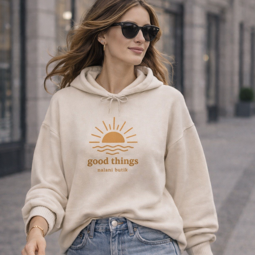 Woman wearing a beige hoodie with a sun graphic and text, walking on a street.