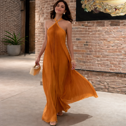 Woman in a long orange dress standing in front of a brick wall.