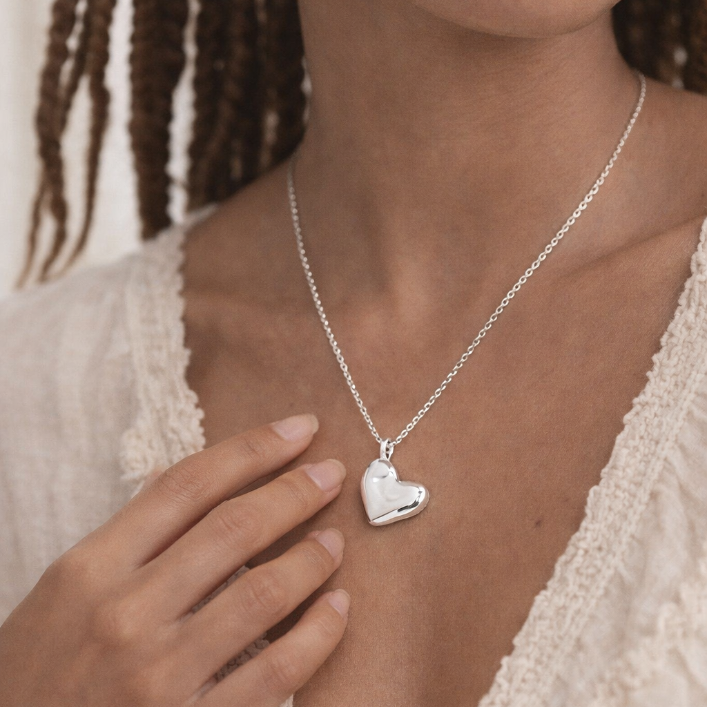 Woman wearing a silver heart-shaped necklace with a neutral background