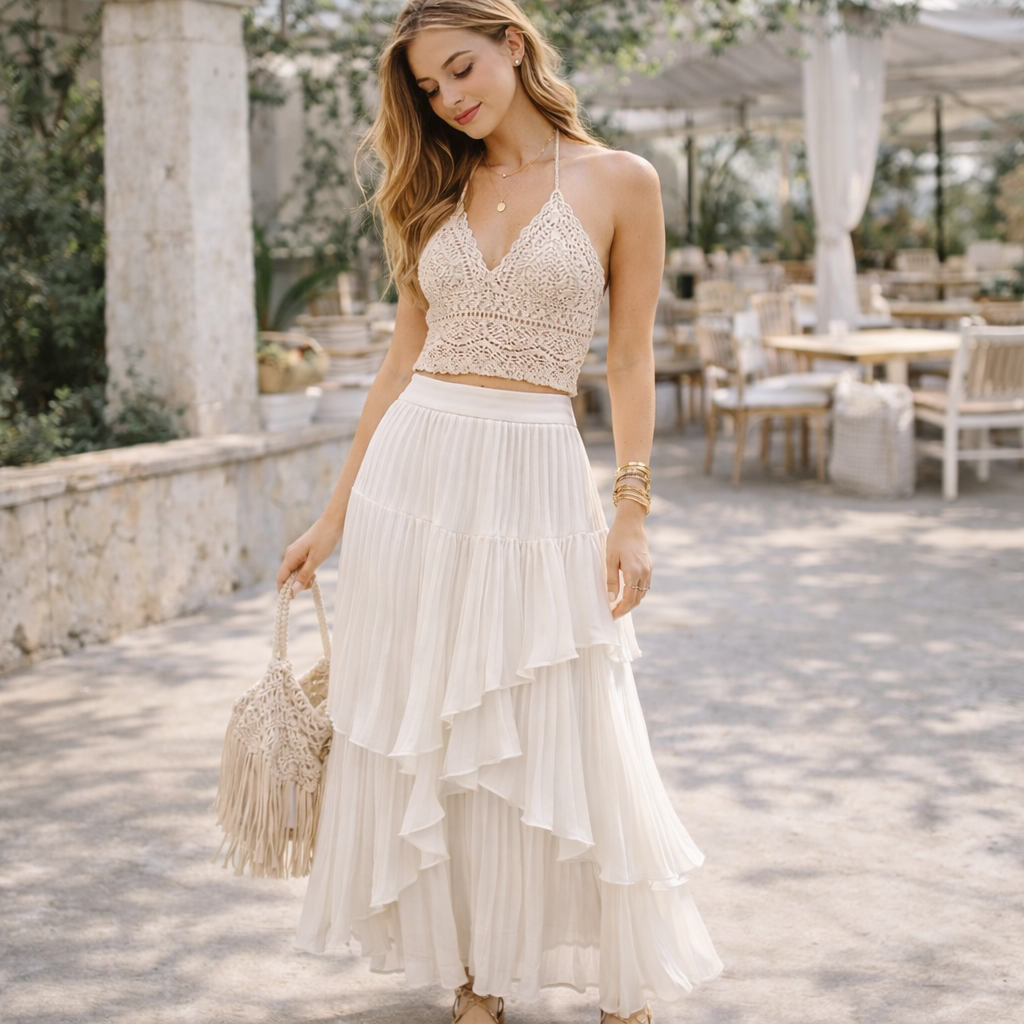 Woman in a beige top and white skirt standing outdoors with tables and chairs in the background.