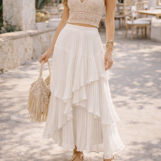 Woman in a white and beige dress standing outdoors with tables and chairs in the background.