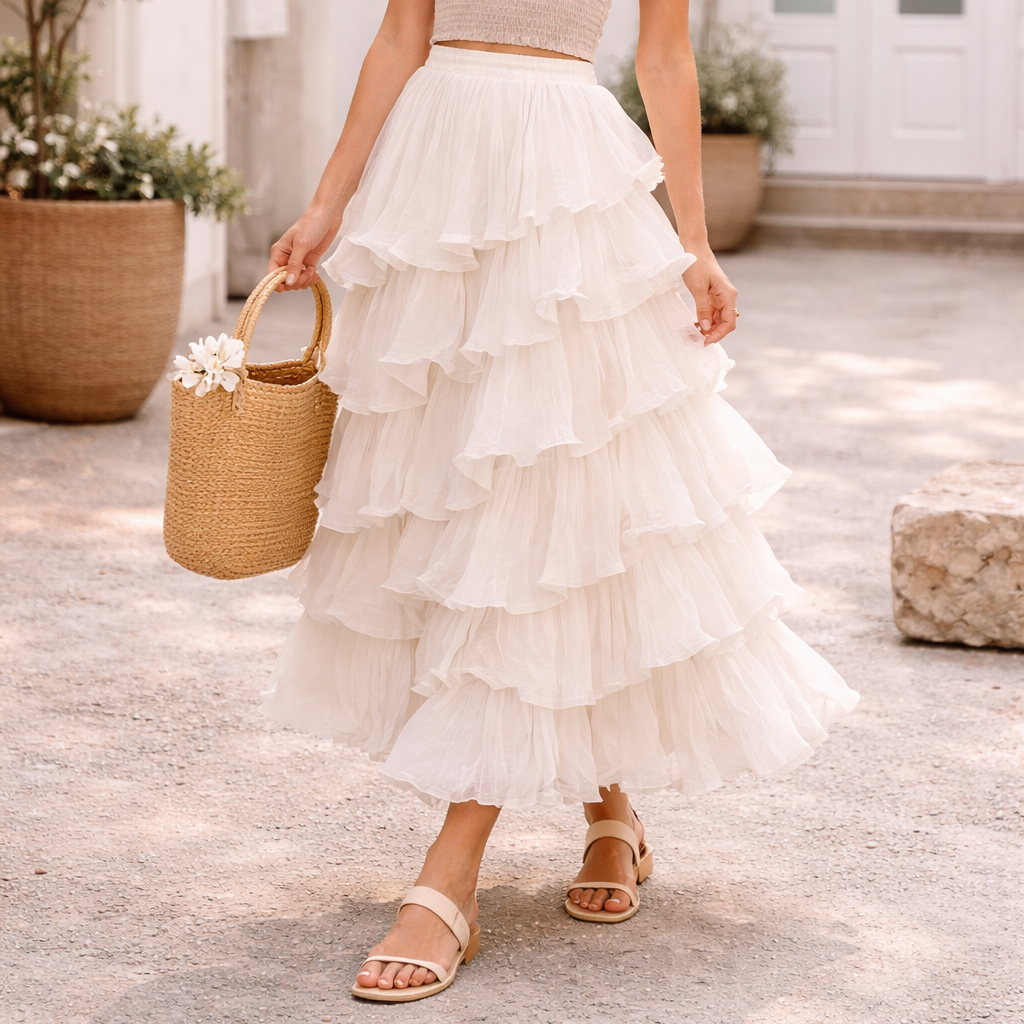 Woman in a beige top and white ruffled skirt holding a straw bag outdoors.